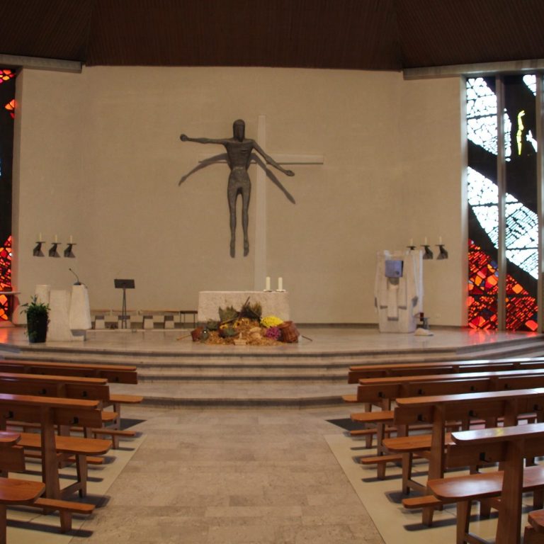 Blick auf den Altar einer Kirche mit Statue und Holzbankreihen.