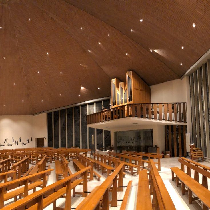 Moderne Kirche mit Holzverkleidung, Sitzbänken und Orgel auf der Empore.