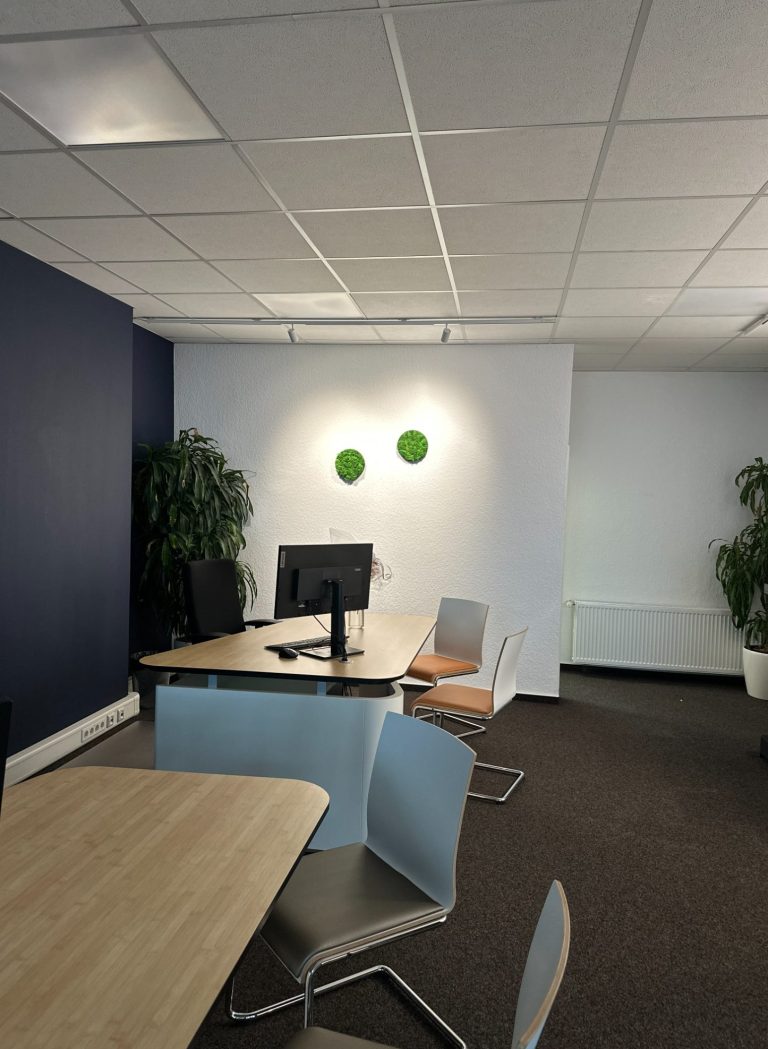 Büro mit Computer, Stühlen und grünen Pflanzen an der Wand.